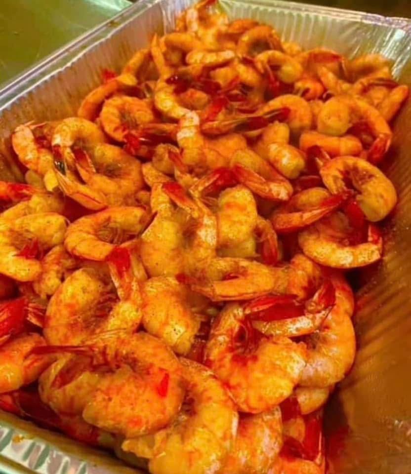 A to-go pan piled with boiled jumbo shrimp in Cajun seasoning